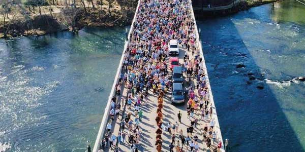 Buddhistische Mönche gehen in einer Reihe über eine Brücke in den USA, begleitet von einer Menschenmenge